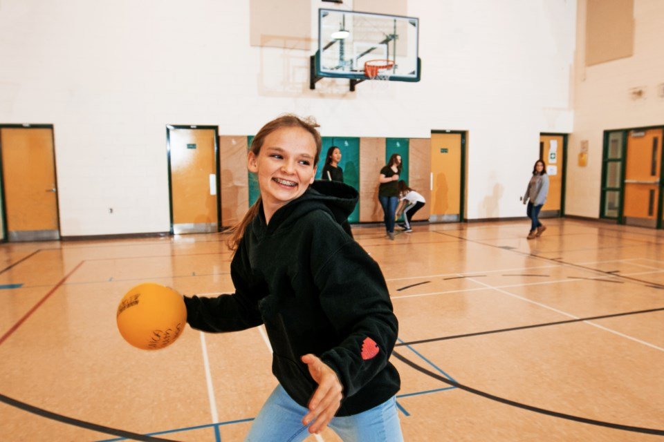 A smiling young player winds up to throw a handball in a Sudbury gym